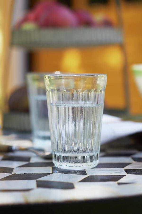A Glass Of Water On A French Bistro Table With A Black And White Diamond Pattern Photograph by Jalag / Olaf Szczepaniak