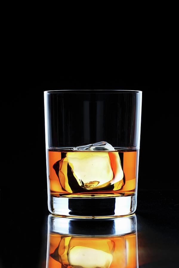 A Glass Of Whiskey With An Ice Cube On A Black Surface Photograph by Perry Jackson