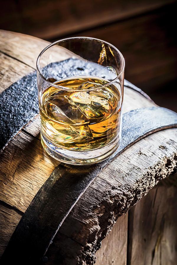 A Glass Of Whiskey With Ice On An Old Wooden Barrel Photograph by Shaiith