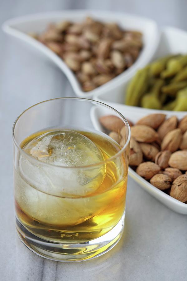 A Glass Of Whisky With A Ball Of Ice And A Selection Of Nuts Photograph by Ernalbant, Emel