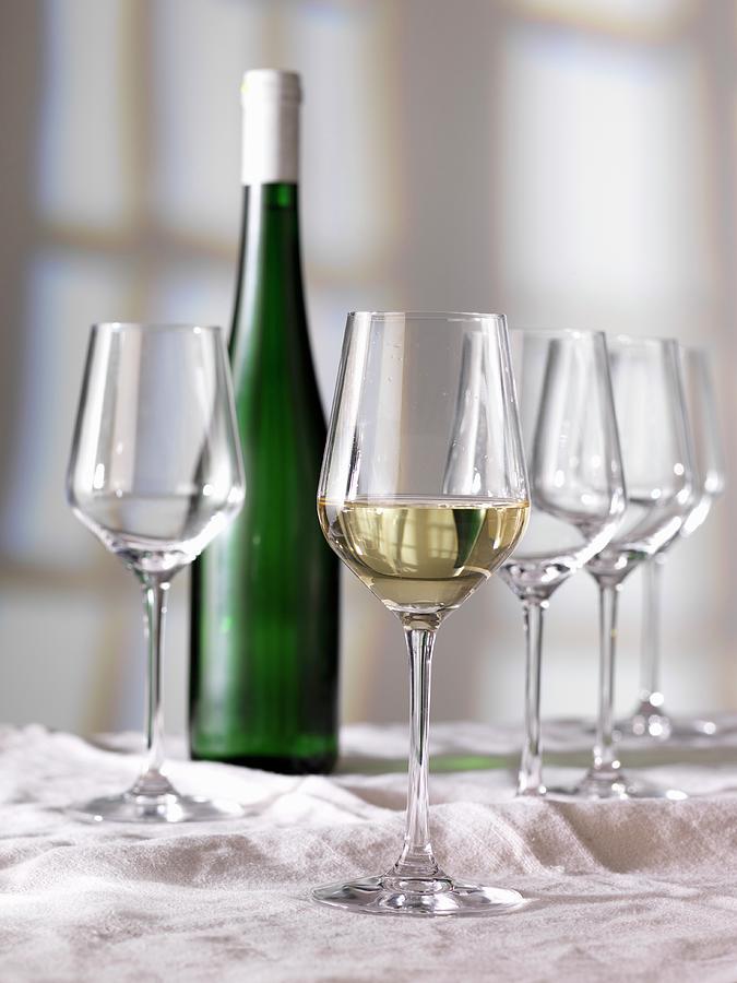 A Glass Of White Wine, A Bottle Of Wine And Empty Glasses Photograph by Ulrike Koeb
