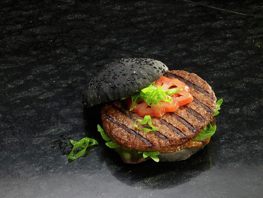 A Grilled Hamburger On A Black Bread Roll Photograph by Nikolai Buroh