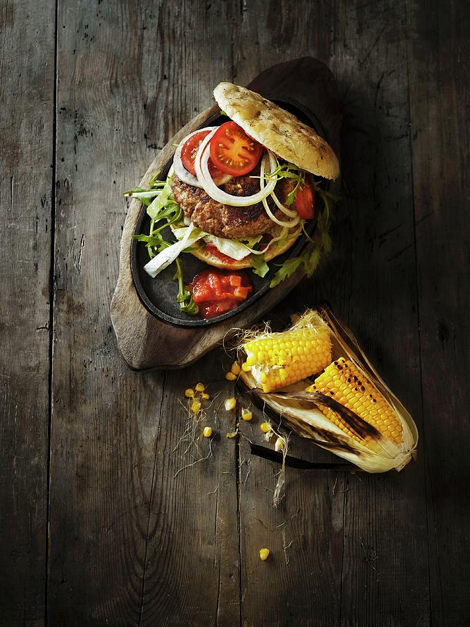 A Hamburger With Tomato Salsa And Grilled Corn Cobs Photograph by Mikkel Adsbl