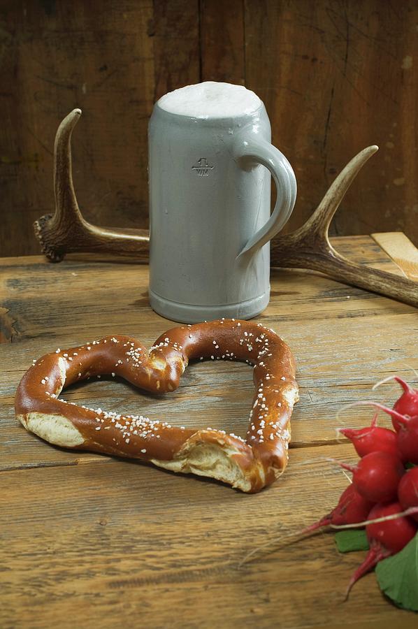 A Heart-shaped Pretzel With Radishes, A Mug Of Beer And Antlers On A Wooden Table Photograph by Achim Sass
