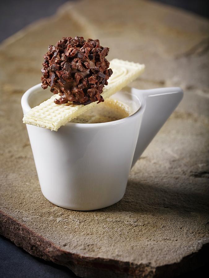 A Homemade Nougat Truffle In Dark Chocolate With Cocoa Bean Splinters On A Cup Of Espresso With A Wafer Photograph by Foto4food