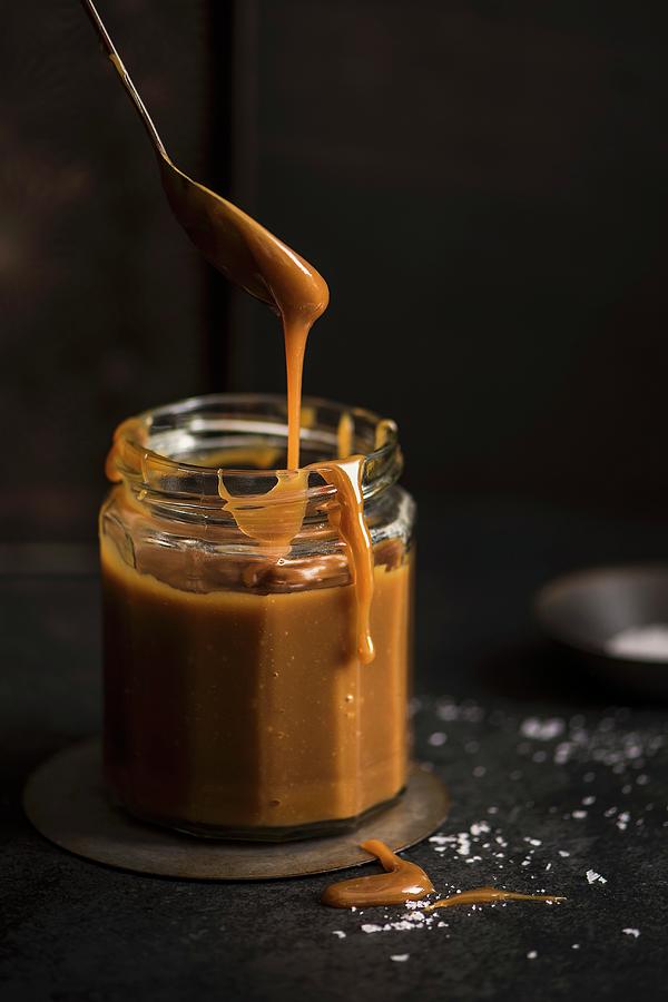 A Jar Of Salted Carmel Sauce With A Spoon, Dark Background Photograph by Magdalena Hendey