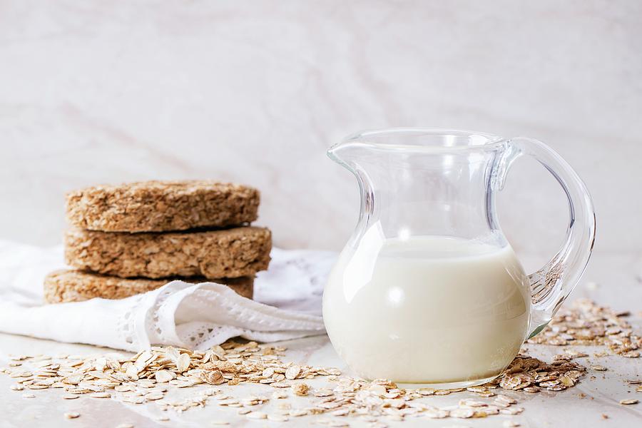A Jug Of Oat Milk, Oats And Crispbread On A White Marble Surface Photograph by Natasha Breen