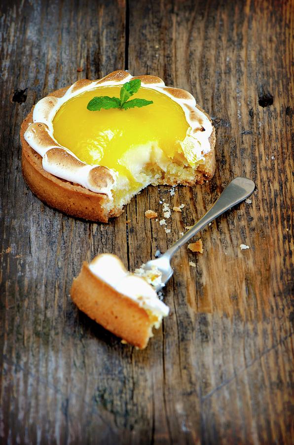 A Lemon Meringue Tartlet On A Wooden Surface With A Bite Taken Out Of It Photograph by Jamie Watson