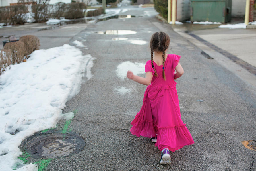Portrait Photograph - A Little Girl In A Fancy Dress Struts Proudly Down A Snowy Street by Cavan Images