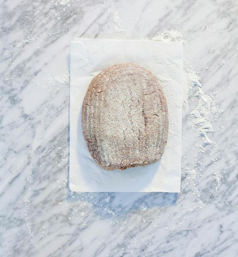 A Loaf Of Bread On Paper, On A Marble Surface, Dusted With Flour Photograph by Achmann, Andreas