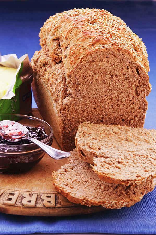 A Loaf Of Bread With Brewers Grains, Two Slices Cut Off, Next To Butter And Jam Photograph by John Hay
