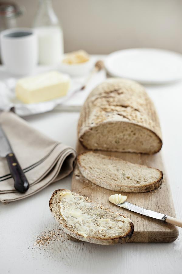 A Loaf Of Sour Dough Bread On A Chopping Board, One Slice Buttered Photograph by Magdalena Hendey
