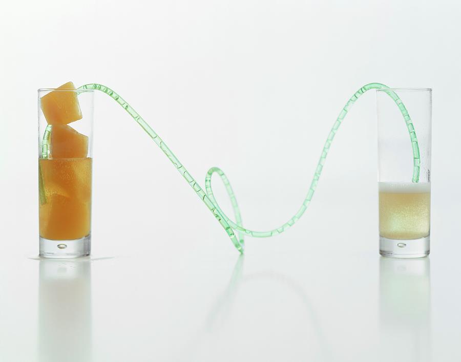 A Long Drinking Straw Connecting A Glass Of Sparkling Wine To A Glass Of Fruit-juice Ice Cubes Photograph by Michael Wissing