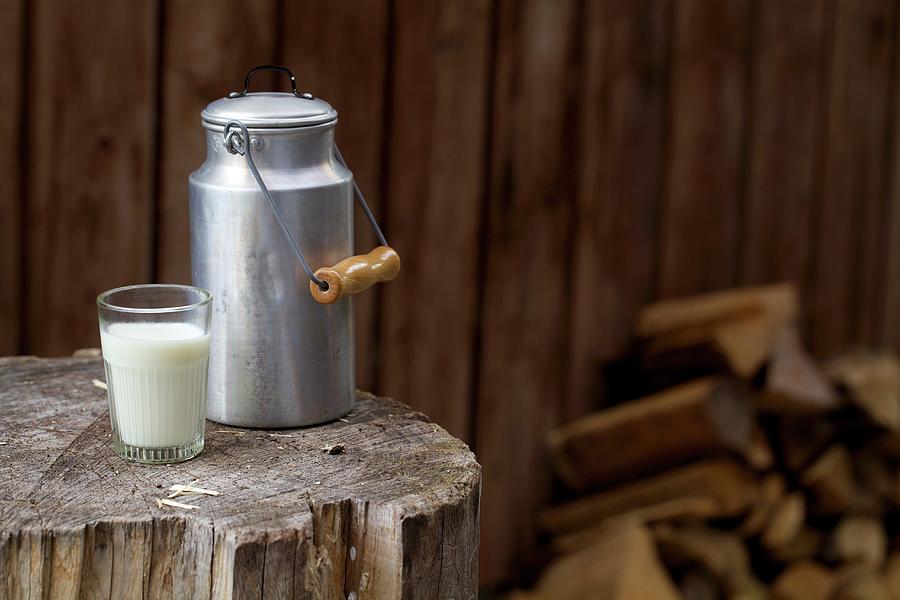 A Milk Churn And A Milk Glass On A Rustic Wooden Block Photograph by Mader, Sabine