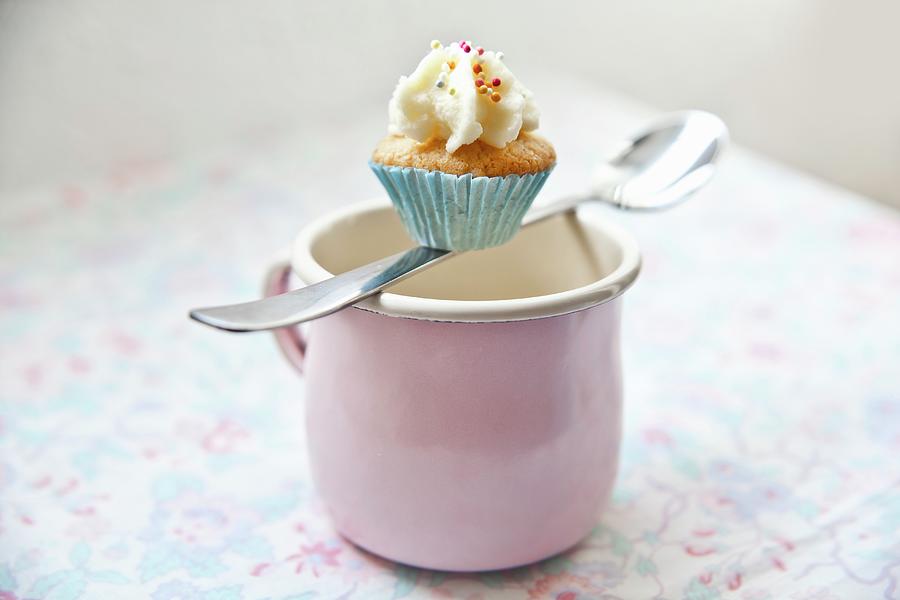 A Mini Cupcake Balanced On A Spoon Over A Pink Enamel Mug Photograph by George Blomfield