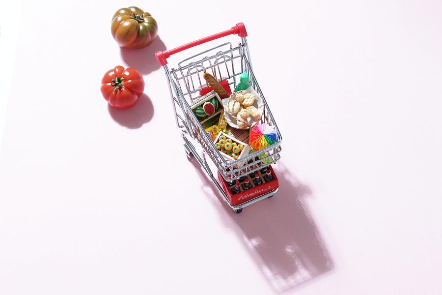 A Mini Shopping Trolley Filled With Toy Foodstuffs Next To Fresh Tomatoes Photograph by Misha Vetter