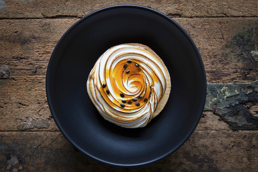 A Passion Fruit Ad Lemon Meringue Tart On A Black Bowl With A Wooden Background Photograph by Andr Ainsworth