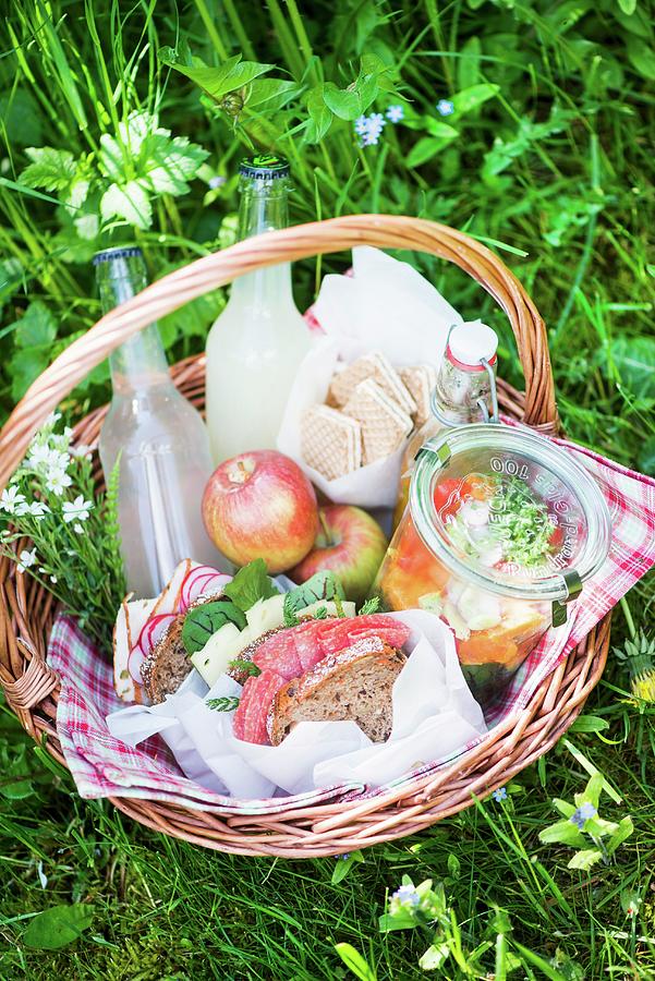 A Picnic Basket With Salami Sandwiches, Salad, Lemonade, Apples And Biscuits Photograph by Fotografie-lucie-eisenmann