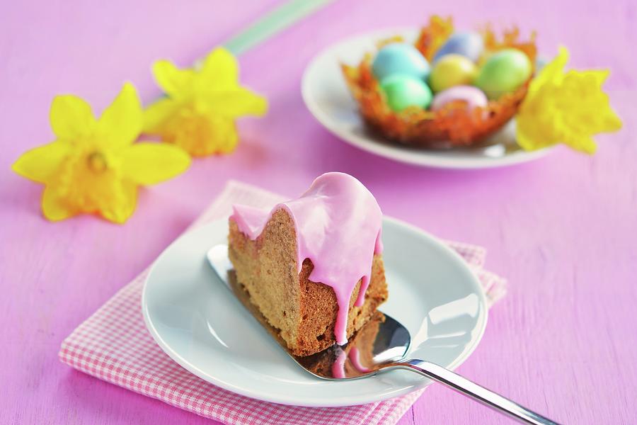 A Piece Of Gugelhupf With A Pink Sugar Glaze, A Caramel Nest With Colourful Sugar Eggs And Daffodils In The Background Photograph by Mariola Streim