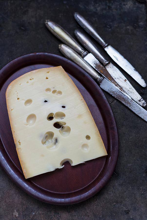 A Piece Of Holey Cheese On A Plate Next To Old Knives Photograph by Adel Bekefi