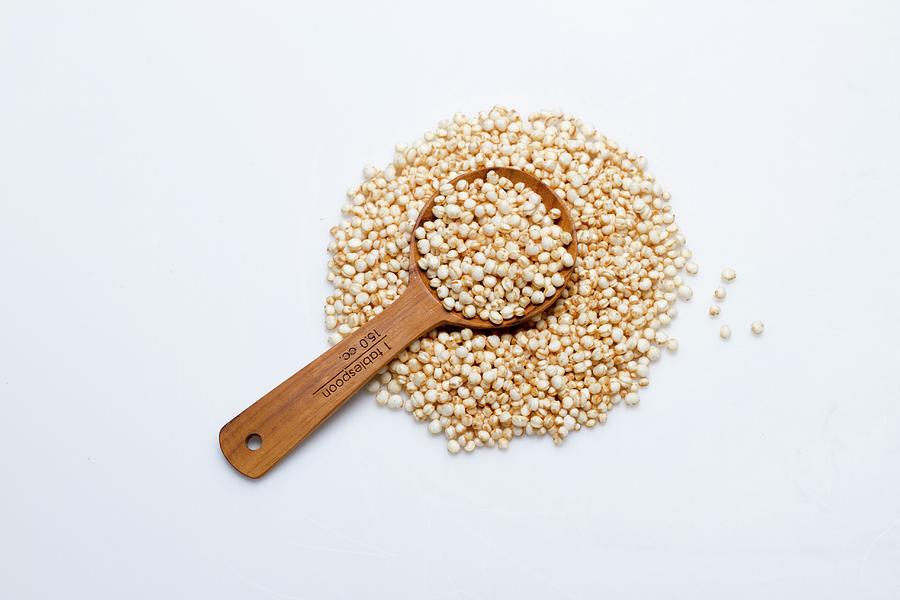 A Pile Of Amaranth Flakes With A Wooden Spoon On A White Surface Photograph by Eising Studio