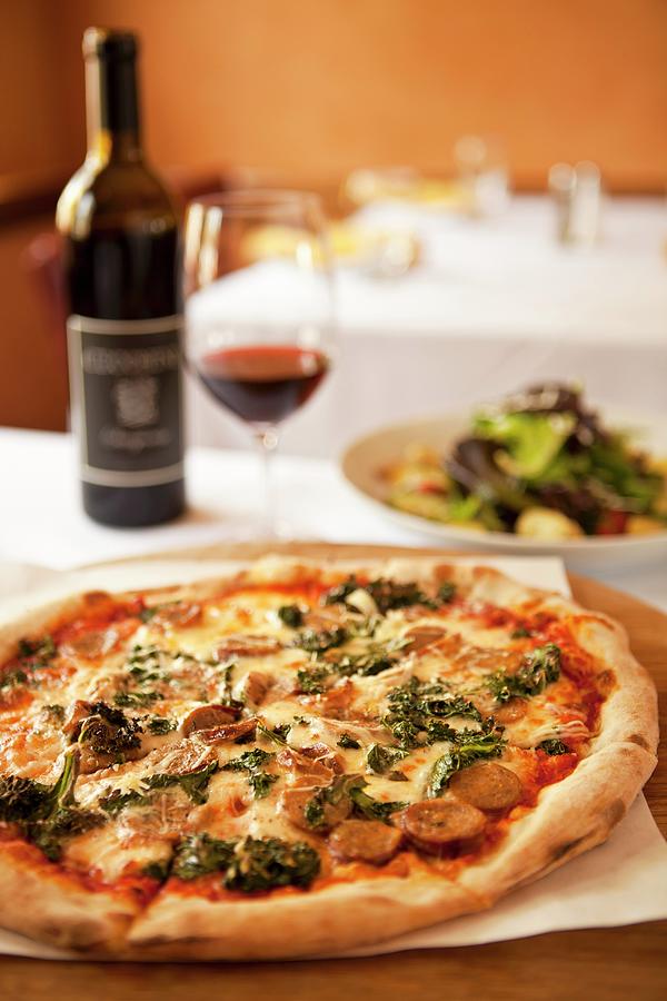 A Pizza Topped With Wild Boar Sausage, Braised Green Kale And Smoked Mozzarella Cheese Served With With Wine And A Salad Photograph by Chuck Place