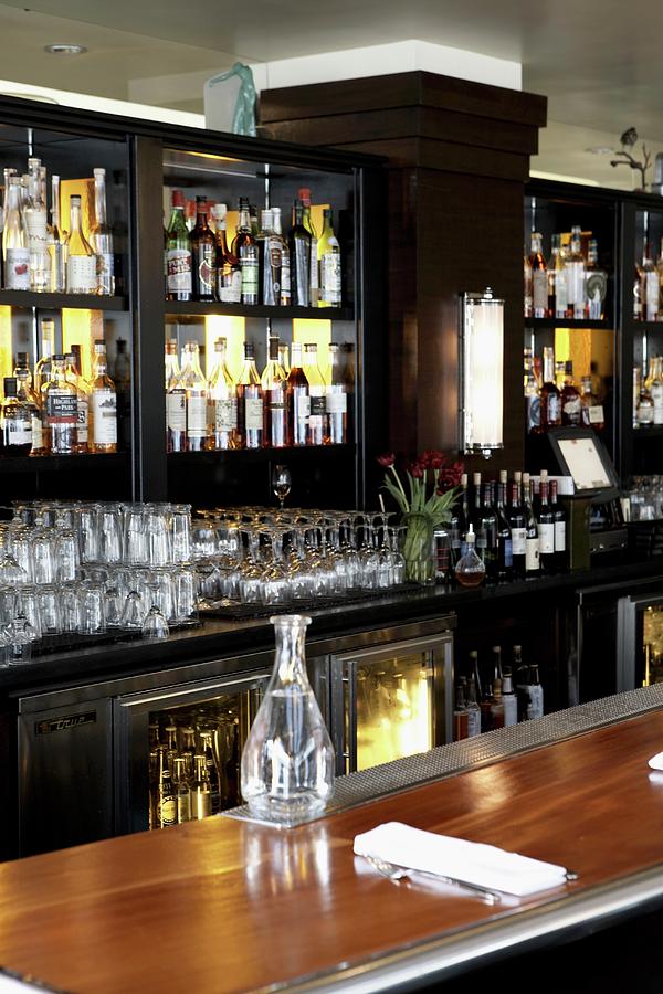 A Polished Wooden Bar In A Restaurant With Shelves Of Spirits And Glasses Behind It Photograph by Cedric Glasier Photography
