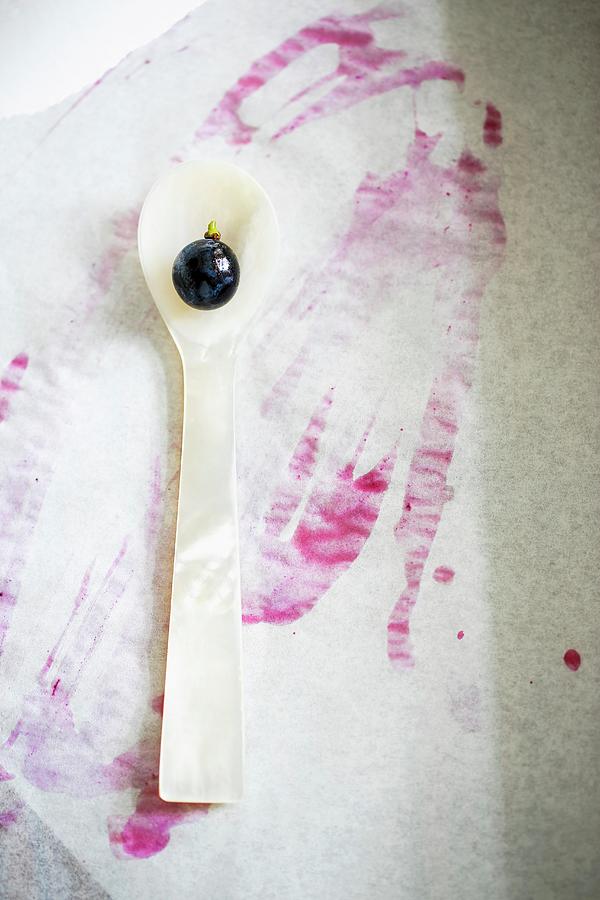A Red Grape On A Mother-of-pearl Spoon With Grape Juice Stains On A Piece Of Paper Photograph by Sandra Krimshandl-tauscher