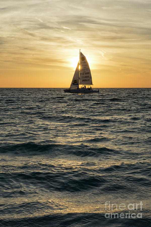 A sailboat crosses the setting sun at sunset at Anna Maria Islan Photograph by William Kuta
