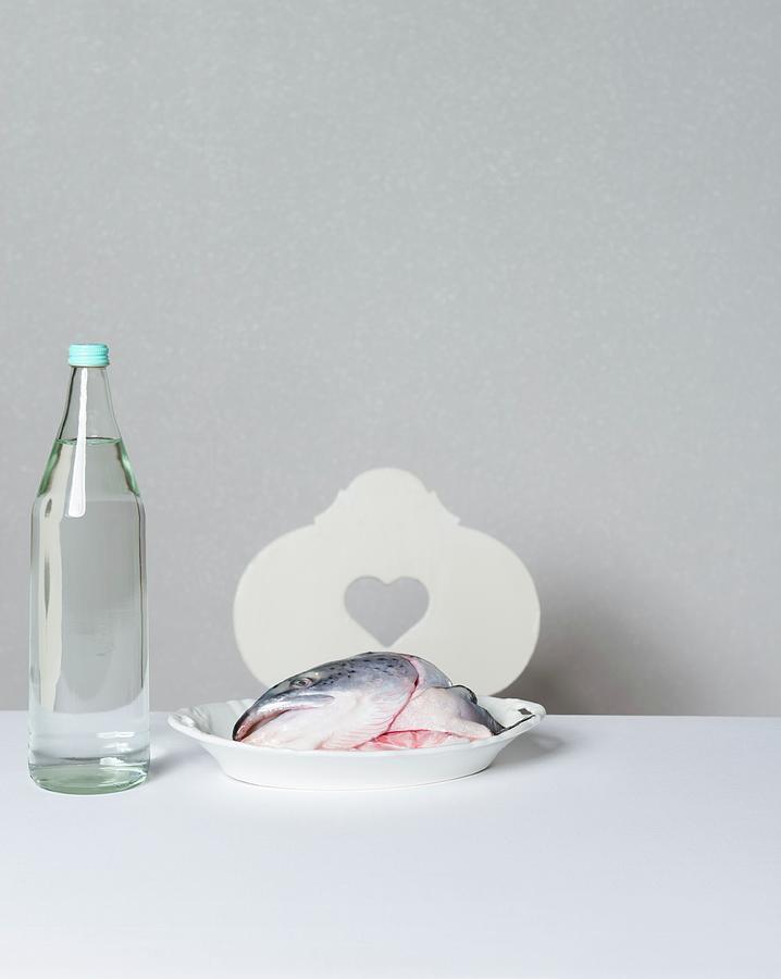 A Salmon Head On A Porcelain Plate Next To A Bottle Of Water Photograph by Angelika Grossmann