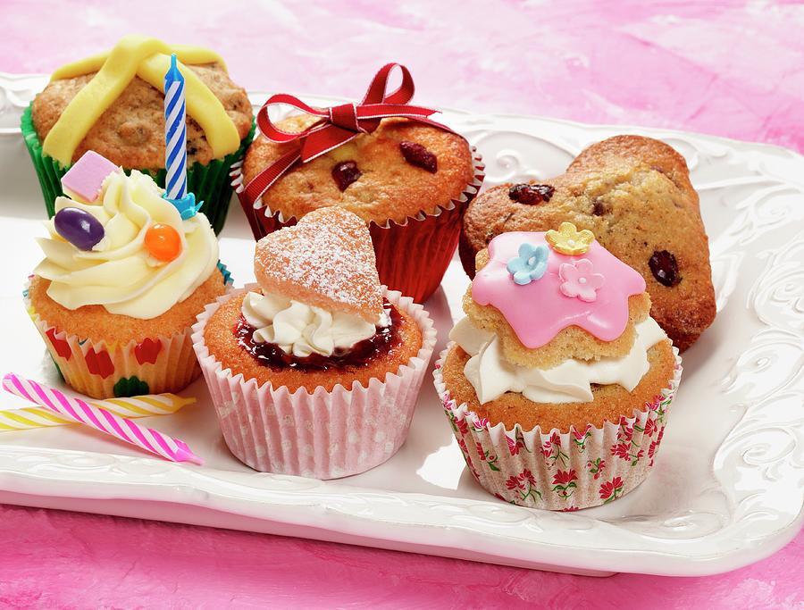 A Selection Of Different Celebration Cupcakes On A Cream Plate And Pink Background Photograph by Stuart Macgregor