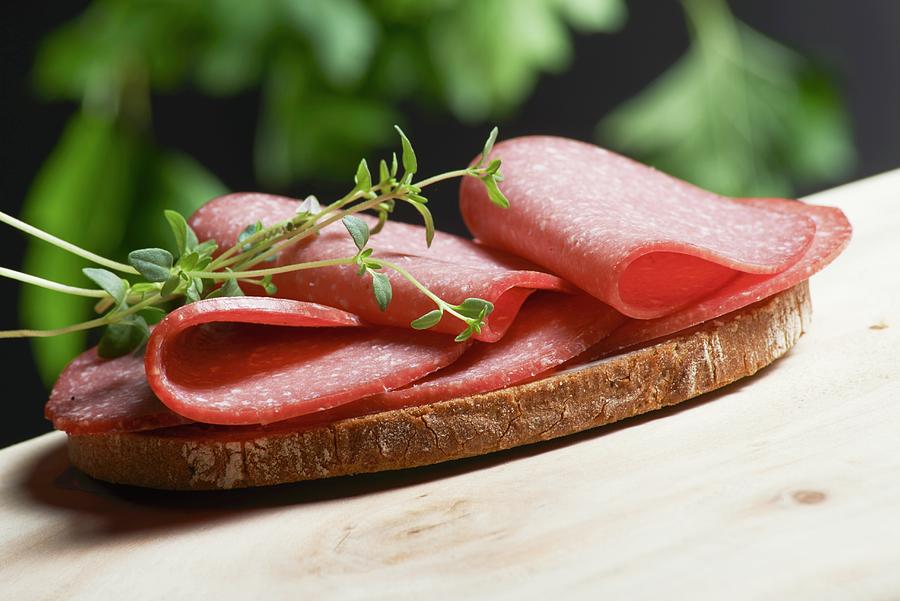 A Slice Of Bread Topped With Salami And Fresh Oregano On A Wooden Table In A Garden Photograph by Brigitte Wegner
