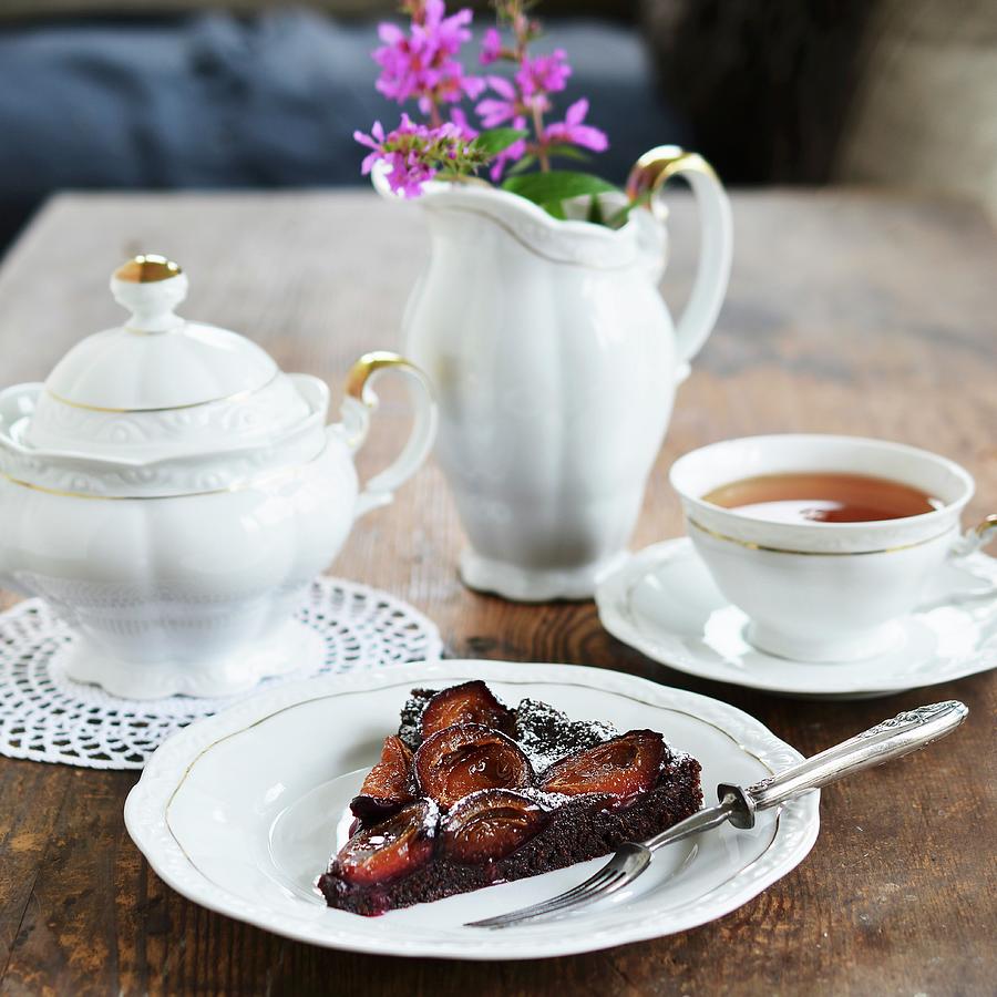 A Slice Of Chocolate Cake With Plums And Icing Sugar Served With Tea Photograph by Mariola Streim