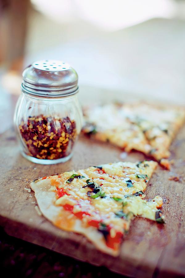 A Slice Of Thin Crust Pizza With A Shaker Of Red Pepper Flakes