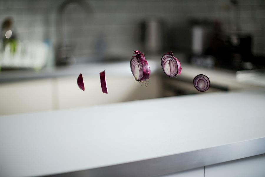 A Sliced Red Onion Floating In Front Of A Kitchen Scene Over A White