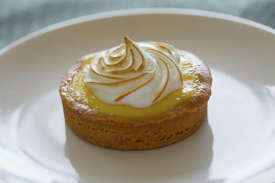 A Small Individual Serving Lemon Tart And Almond Crust With Meringue Topping On A White Plate Photograph by Albert P Macdonald