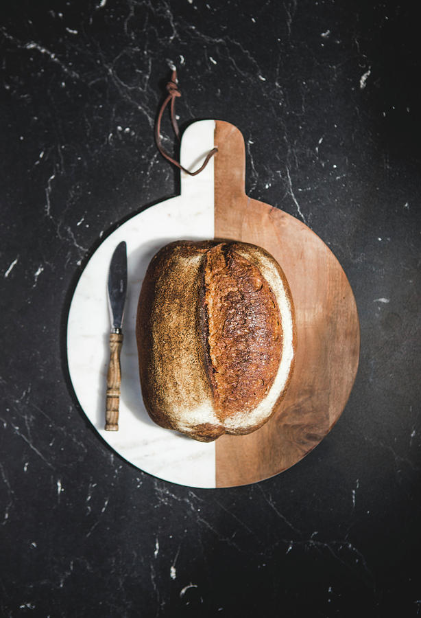 A Small Loaf Of Bread With A Knife On A Brown-and-white Wooden Chopping Board seen From Above Photograph by Karolina Kosowicz