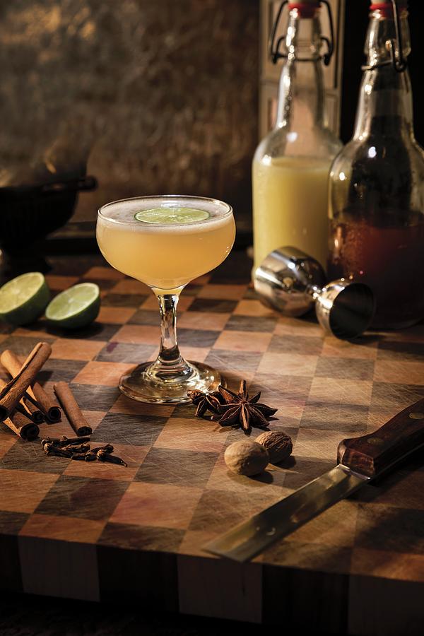 A Spicy Ginger Cocktail Garnished With A Slice Of Lime And Surrounded By Star Anise, Cinnamon, Cloves And Nutmeg Photograph by Cindy Haigwood