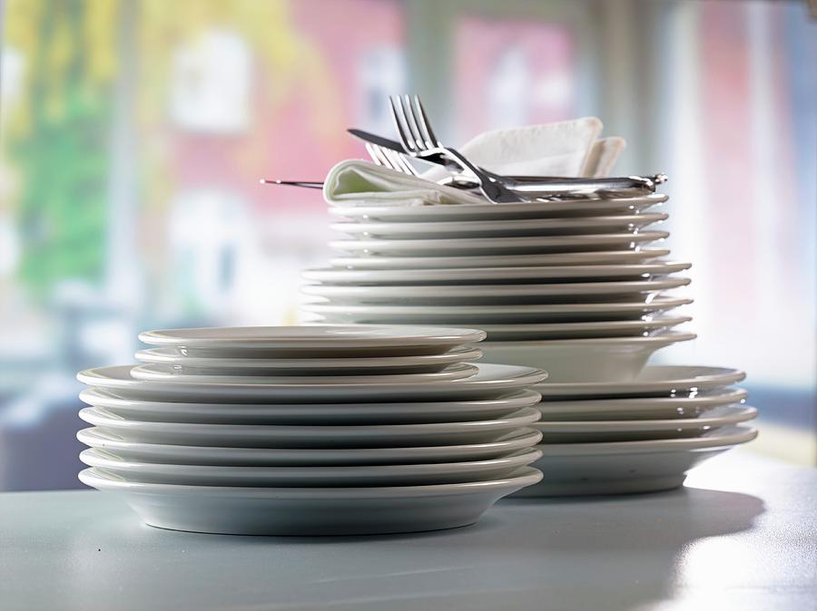 A Stack Of Plates And Fabric Napkins With Cutlery In Front Of A Kitchen Window Photograph by Ludger Rose