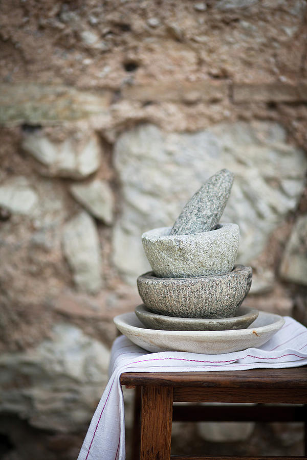 A Stack Of Stone Mortars With A Pestle In Front Of A Stone Wall Photograph by Eising Studio