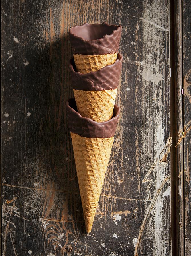 A Stack Of Three Chocolate Dipped Ice Cream Cones On A Wooden Surface Photograph by Stacy Grant