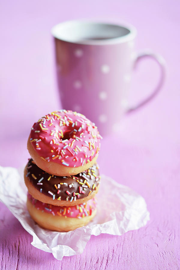 A Stack Of Three Mini Doughnuts With Icing And Sugar Strands In Front Of A Teacup Photograph by Mariola Streim