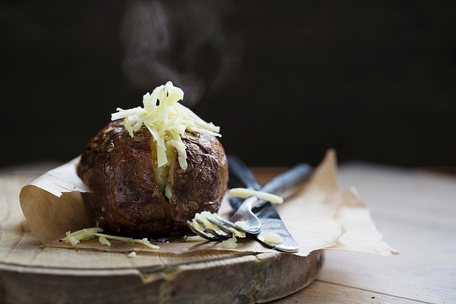 A Steaming Baked Potato With Cheese On A Piece Of Baking Paper Photograph by Cath Lowe