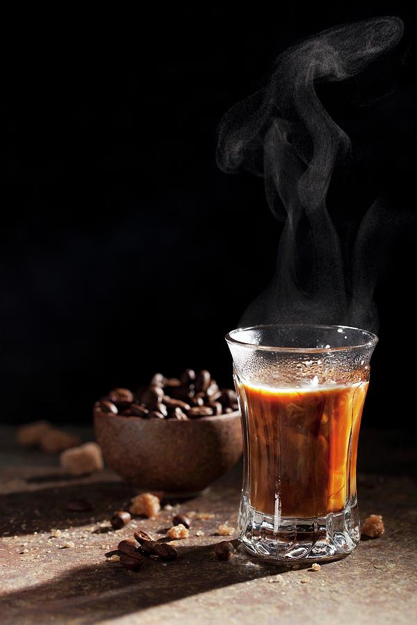 A Steaming Glass Of Coffee With Coffee Beans And Sugar Lumps In The Background Photograph by Jane Saunders