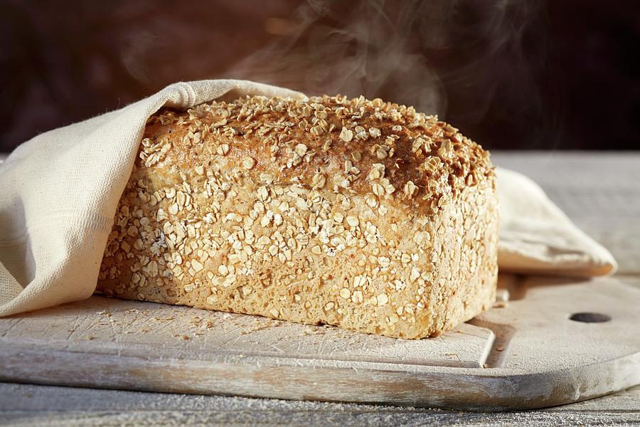 A Steaming Loaf Of Spelt-chia Bread On A Chopping Board Photograph by Niklas Thiemann