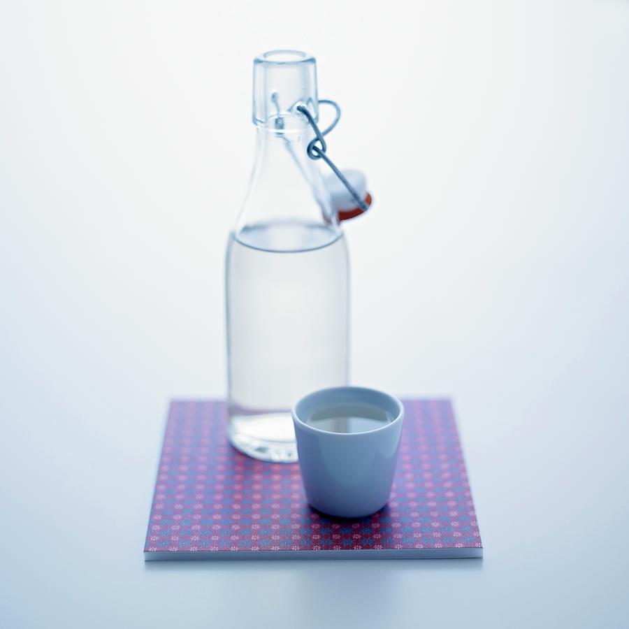 A Stoppered Bottle And A Cup Of Water Photograph by Will Shaddock Photography