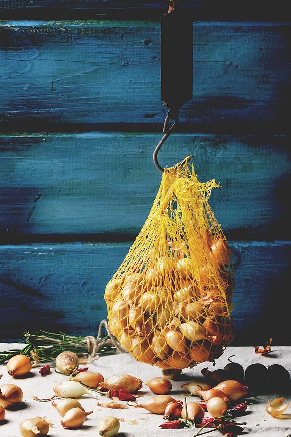 A String Bag Of Small Onions Against A Wooden Wall Photograph by Natasha Breen