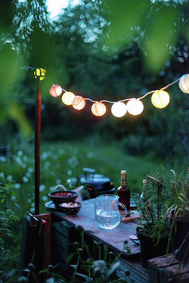 A String Of Lanterns Above A Rustic Garden Table With Drinks And Snacks Photograph by Sebastian Schollmeyer