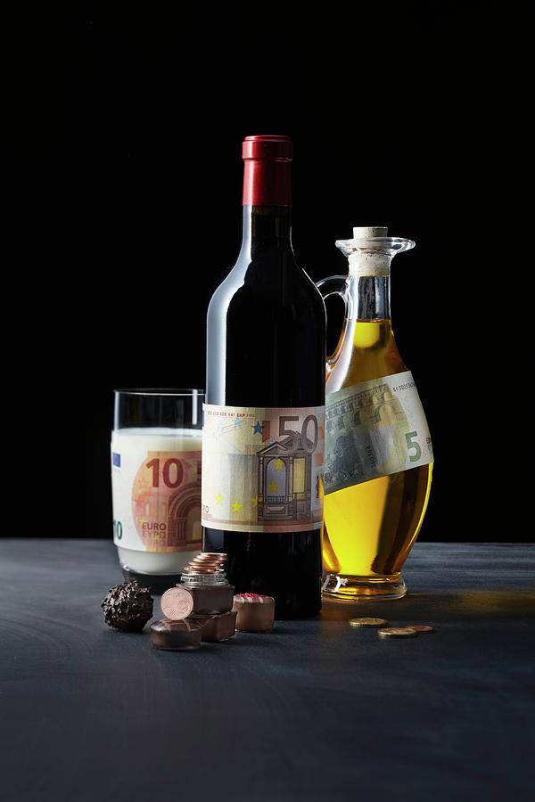 A Symbolic Image Of A Gourmet Investment: Pralines, Red Wine, Milk And Olive Oil With Money Photograph by Jalag / Gtz Wrage