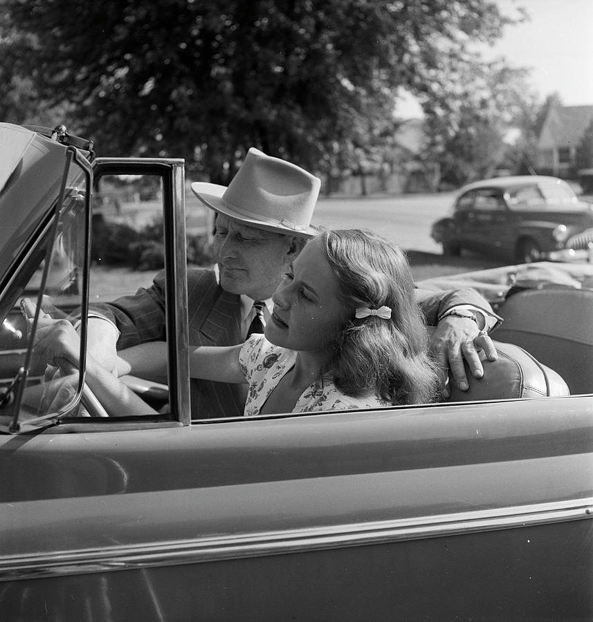 A teenage girl sitting behind the wheel of a car while an unidentified man is sitting nearby in Tulsa, OK in 1947. Photograph by Nina Leen